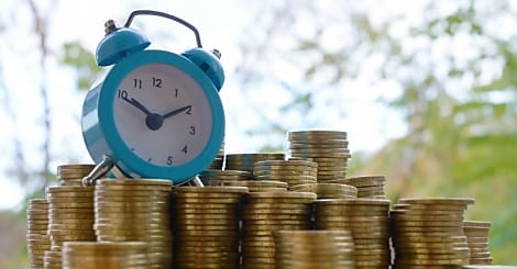 Blue alarm clock on big amount of shiny ukrainian old 1 hryvnia coin stacks clos