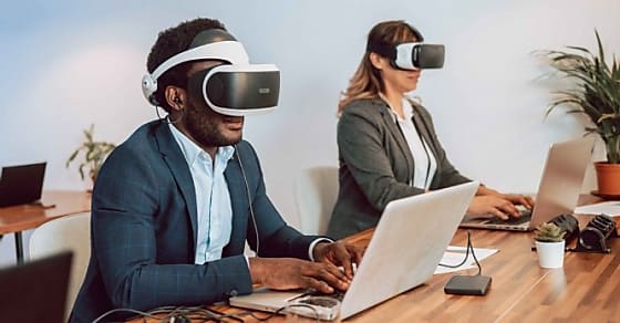 Concentrated African American male entrepreneur in VR goggles sitting at table w