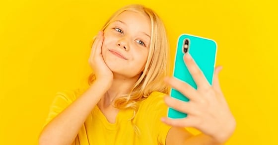 Smiling little girl kid showing blue screen of new popular mobile phone on light