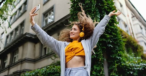 Portrait of young woman with smartphone dancing outdoors on street, tik tok conc