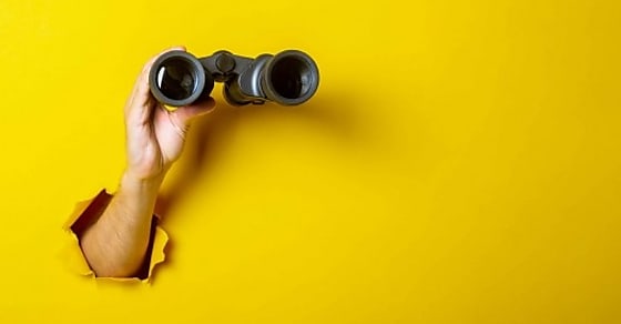 Female hand holds black binoculars on a yellow background. Looking through binoc