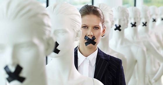 A woman standing in line of mannequins with taped mouth
