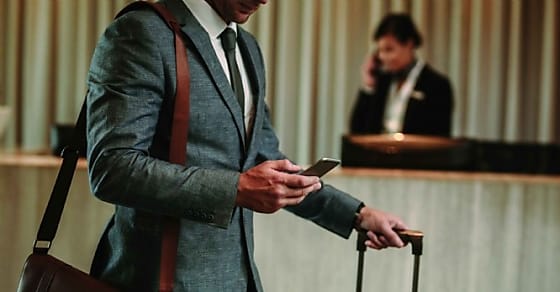 cropped shot of businessman in hotel lobby with mobile phone and luggage. Male b